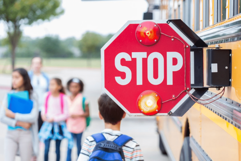 Stock image of a school bus stop sign with children in the backgroun.